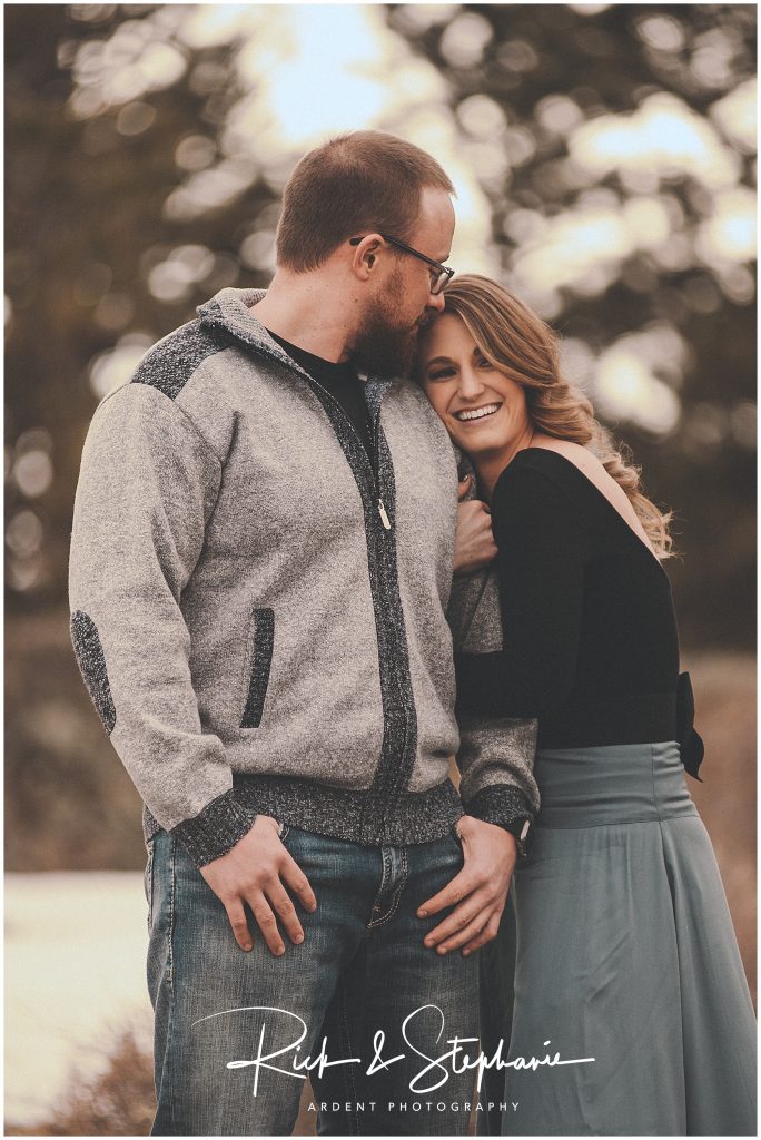 Engaged couple cuddle in getting warm during their Wyoming engagement session. Wintry mountain scenery is in the background.